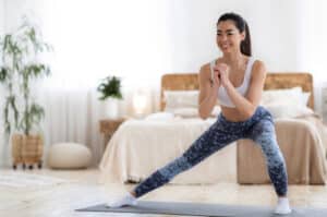 Happy Sporty Asian Woman Doing Lunges Exercises On Mat In Bedroom 1