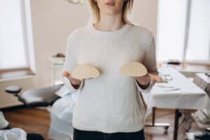 Close up of a woman holding two breast implants in front of her chest, trying to choose the right option