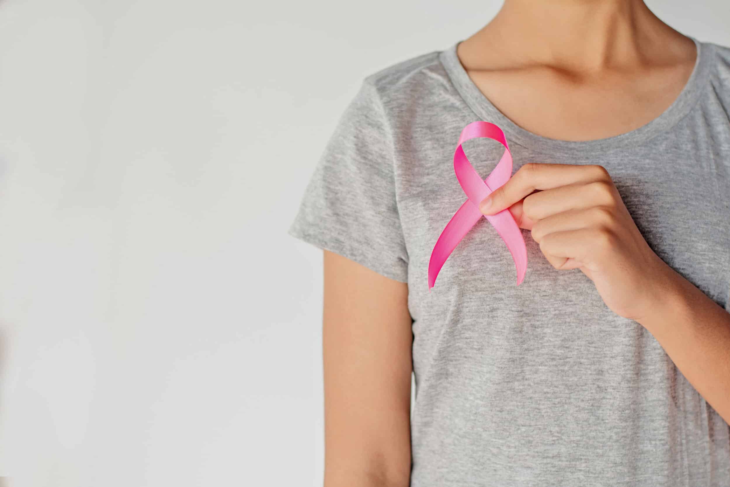 Woman in gray t-shirt holding up pink breast cancer ribbon