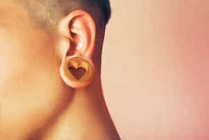 Close-up of a stretched earlobe with a wooden gauge featuring a heart-shaped cutout