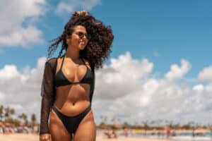 Woman in a black bikini at the beach, featured in a blog about breast implant placement options.