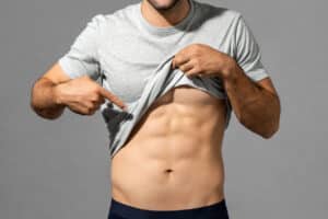 Man lifting his shirt to show a toned abdomen, featured in a blog about male tummy tuck surgery.