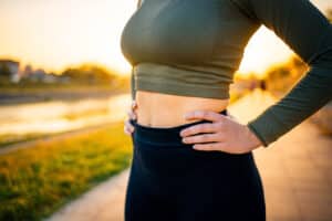 Fit woman in athletic clothing with hands on her hips, featured in a blog about skin elasticity and liposuction candidacy.